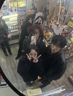 three people standing in front of a store looking at their cell phones and making the peace sign