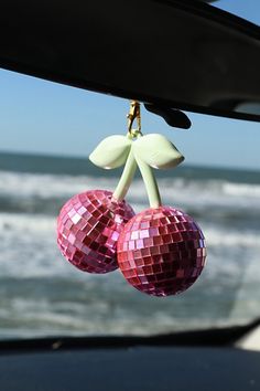 two disco ball ornaments hanging from the side of a car near the ocean and waves