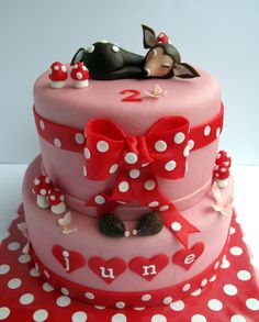 a pink cake with white polka dots and red bows on the top is topped with a sleeping dog