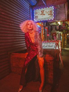 a woman sitting on top of a wooden bench in front of a neon lit building