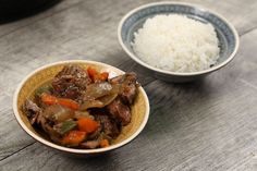 two bowls filled with rice and meat on top of a wooden table