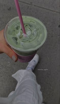 a person holding a drink with a pink straw in it's hand and wearing white sneakers