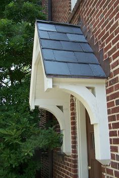 a brick building with a black roof and white trim on the front door is next to a green tree