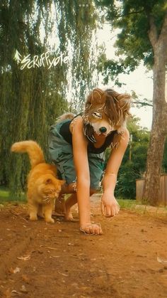 a young child is playing with a cat in the dirt near some trees and grass