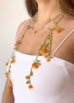 a woman wearing a white top with orange flowers attached to her chest and green leaves on it