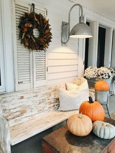 a wooden bench sitting in front of a white house with pumpkins on the ground