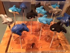 there are many blue and black animal cake pops on the wooden board with toothpicks in them