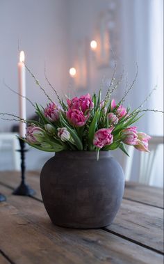 a vase filled with pink flowers sitting on top of a wooden table next to a lit candle