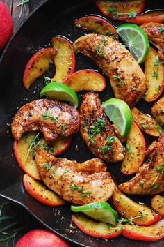 a skillet filled with chicken, apples and limes on top of a wooden table