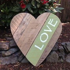 a wooden heart with the word love painted on it sitting in front of some flowers