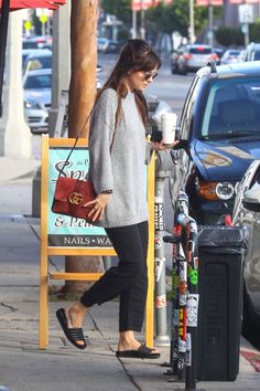 a woman is walking down the sidewalk with her hand in her pocket and holding a coffee cup