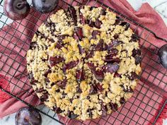 a pie sitting on top of a cooling rack next to plums