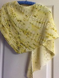 a yellow knitted shawl hanging on a white door with a blue ribbon around it