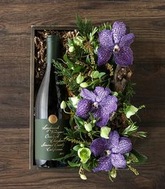 a bottle of wine in a box with purple flowers and greenery on the side