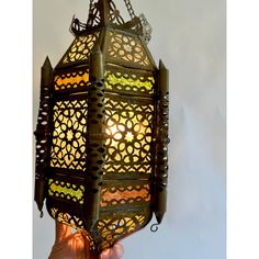 a hand holding up a decorative lantern with the light shining on it's side