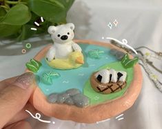 a hand is holding a small figurine in the shape of a fish pond