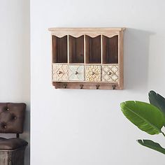 a wooden shelf with four compartments on the wall next to a brown chair and potted plant