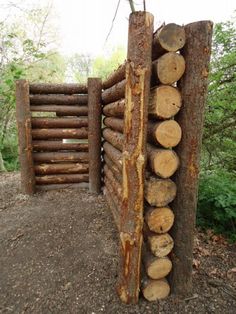 logs stacked on top of each other in front of a wooden gate with trees growing out of it