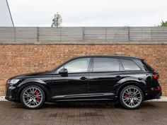 a black suv parked in front of a brick wall with red rims on it