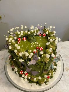 a heart shaped cake with white flowers and green leaves on top is sitting on a table