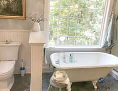 a white bath tub sitting next to a toilet in a bathroom under a large window