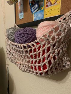 there is a crochet bag hanging on the wall with yarn in it and two balls of yarn inside