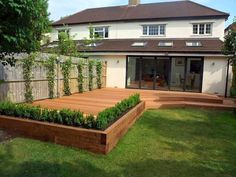 a wooden deck in front of a white house with green grass and trees around it