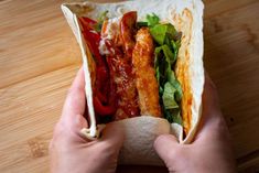 a person holding a wrap filled with meat and veggies on top of a wooden table