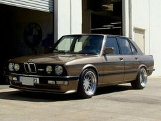 a brown bmw is parked in front of a garage with its door open and it's hood up