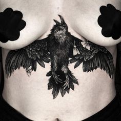 a woman's stomach with black and white tattoos on her chest, showing an image of a bird