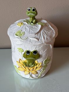 a ceramic frog sitting on top of a flower pot with leaves and flowers painted on it