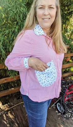 a woman standing on a wooden deck wearing a pink and white striped shirt with floral appliques