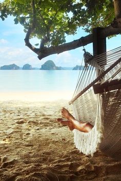 a person laying in a hammock on the beach with their feet propped up