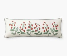 a white pillow with red berries and green leaves on the front, sitting on a white surface