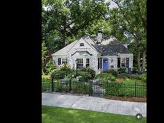 a white house with blue doors and windows in front of a black fenced yard