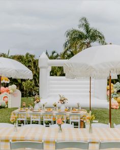 an outdoor table set up with yellow and white checkered cloths, umbrellas, and flowers