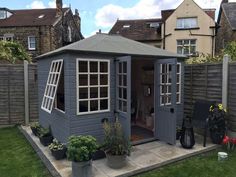 a small gray shed with windows and potted plants in the back yard next to a fence