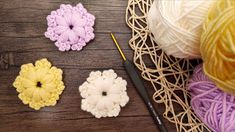 three crochet flowers sitting on top of a wooden table next to yarn and knitting needles