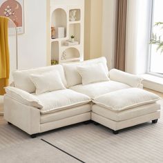 a living room with a large white sectional couch and pillows on the bottom half of it