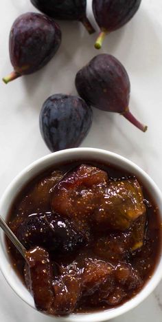 a white bowl filled with plum sauce next to some figs on a marble counter