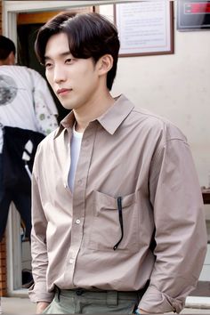 a young man standing in front of a building wearing a tan shirt and khaki pants