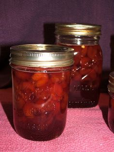 three jars filled with pickles sitting on top of a pink table cloth next to each other