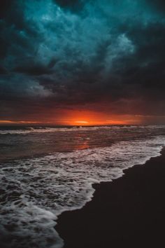 the sun is setting over the ocean with dark clouds in the sky and waves on the beach