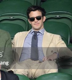 two men sitting next to each other in front of green seats wearing sunglasses and suits