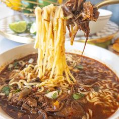 a bowl of noodles being lifted with chopsticks