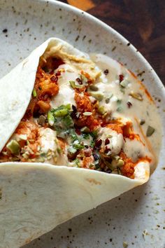 a tortilla filled with meat, cheese and sauce on top of a white plate