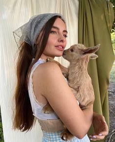 a woman holding a baby goat in her arms and wearing a hat on top of her head