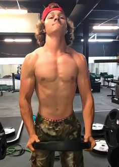 a man with no shirt on standing in front of a gym machine and looking up at the sky