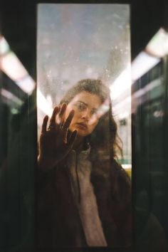 a woman standing in front of a window holding her hand up