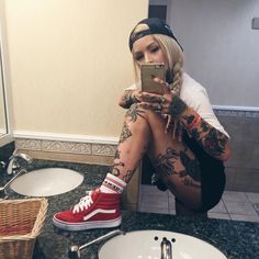 a woman with tattoos sitting on the ground looking at her cell phone in a bathroom